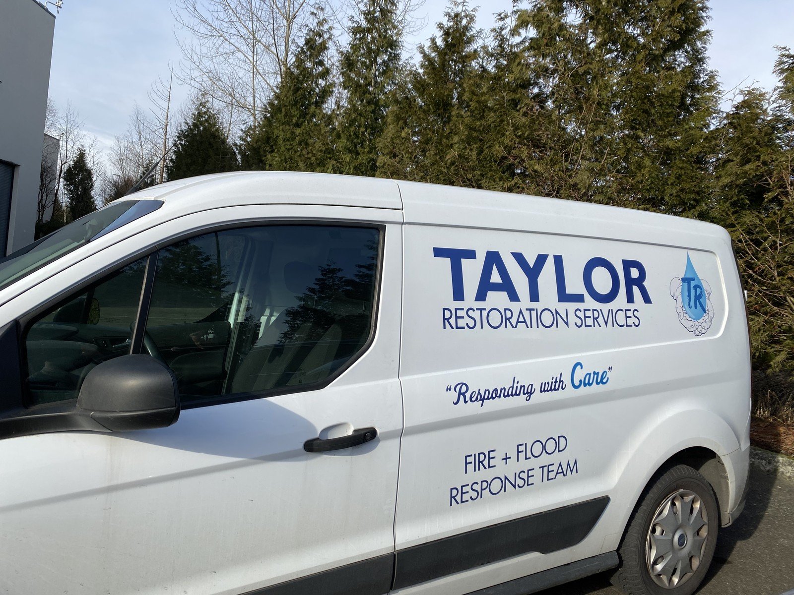 Close-up of the side of a small Taylor Restoration Services van, showing the company name, water-droplet logo, the tagline "Responding with Care" and Fire + Flood Response Team lettering.