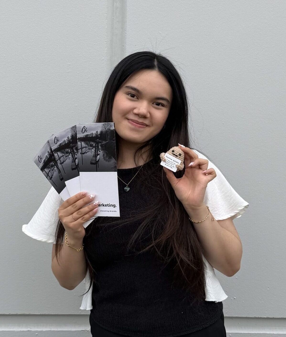 An Oi Marketing team member holding a fan of printed Oi Marketing tri-fold brochures reading 'elevating brands,' alongside a small crocheted toy.