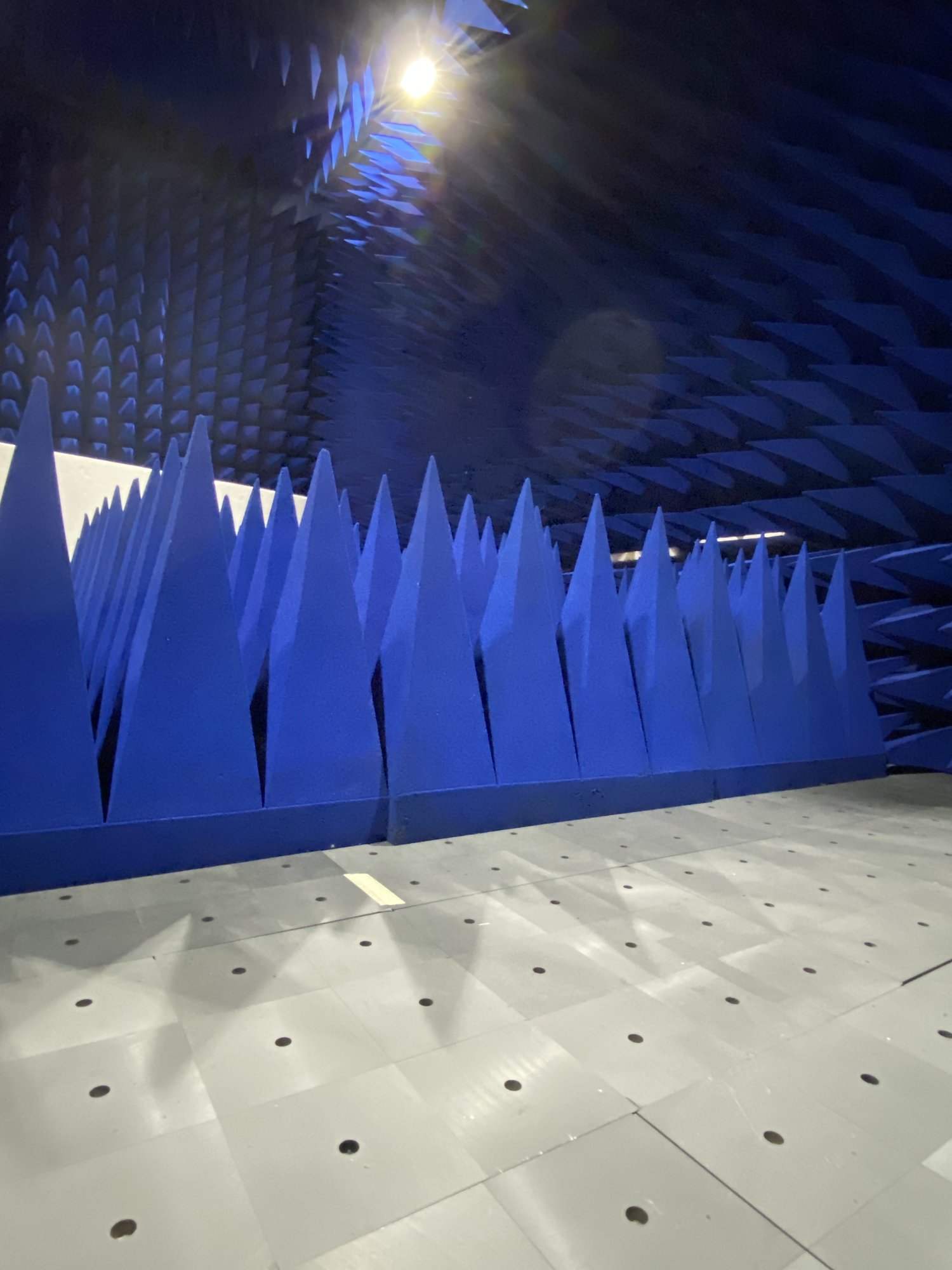 A corner of the anechoic test chamber at LabTest Certification, with rows of blue radio-frequency absorber cones above a perforated metal ground-plane floor.