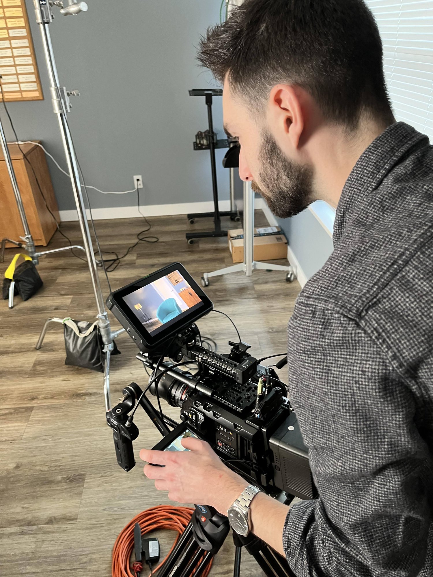 A Dream It Creations camera operator adjusting a cinema camera rig fitted with an external monitor, on an indoor set with C-stands and cabling.