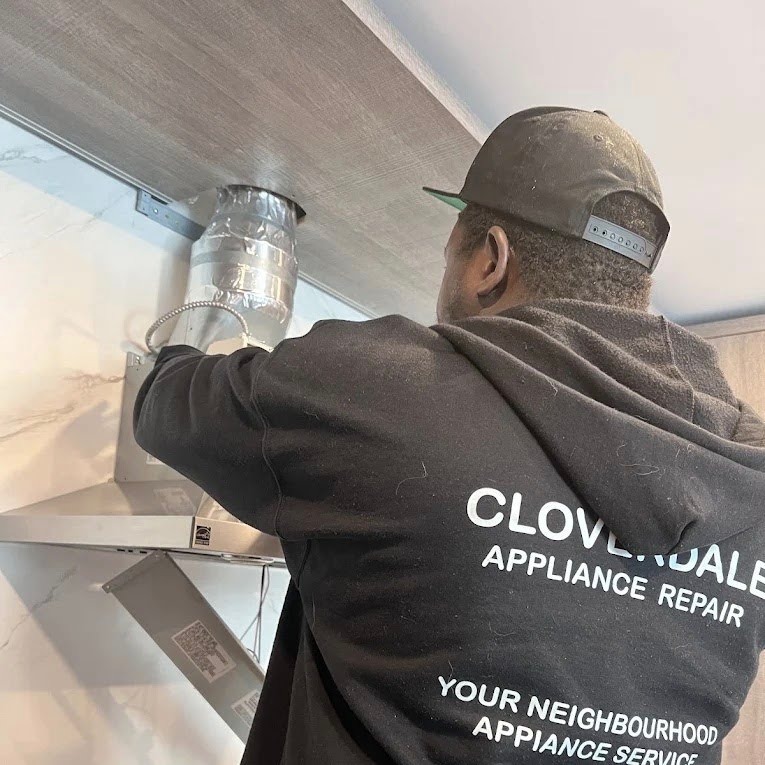 A Cloverdale Appliance Repair technician in a branded company hoodie installing a kitchen range hood duct system.