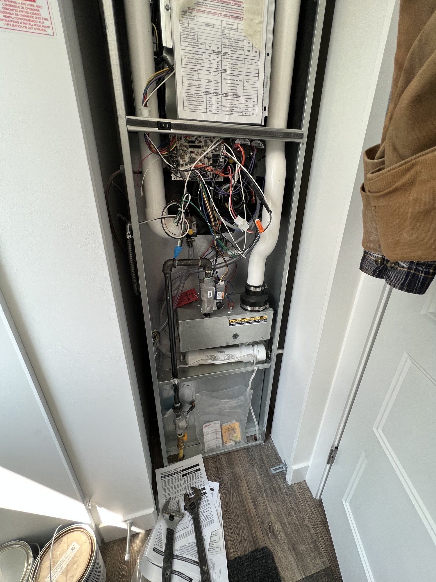A gas furnace in a narrow utility closet with its front panel removed, exposing the control board, wiring harness and gas valve during service